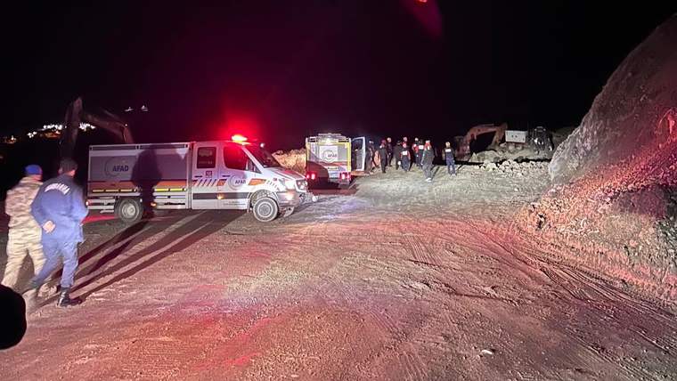 Gece, kırmızı ışıkları yanan ambulanslar ve iş makinelerinin bulunduğu kayalık alanda insanlar bekliyor.