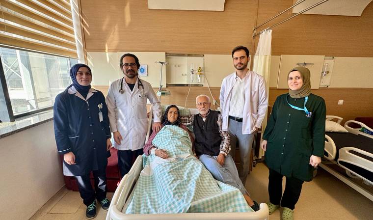 Hastane odasında, hasta kadın ve doktorlar ile aile üyeleri birlikte poz veriyor.