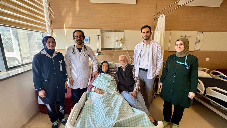 Hastane odasında, hasta kadın ve doktorlar ile aile üyeleri birlikte poz veriyor.