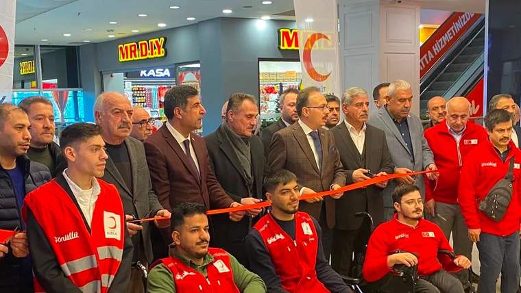 Kızılay yazılı kırmızı yelekli kişiler, alışveriş merkezinde tekerlekli sandalyedeki üç kişinin önünde duruyor.
