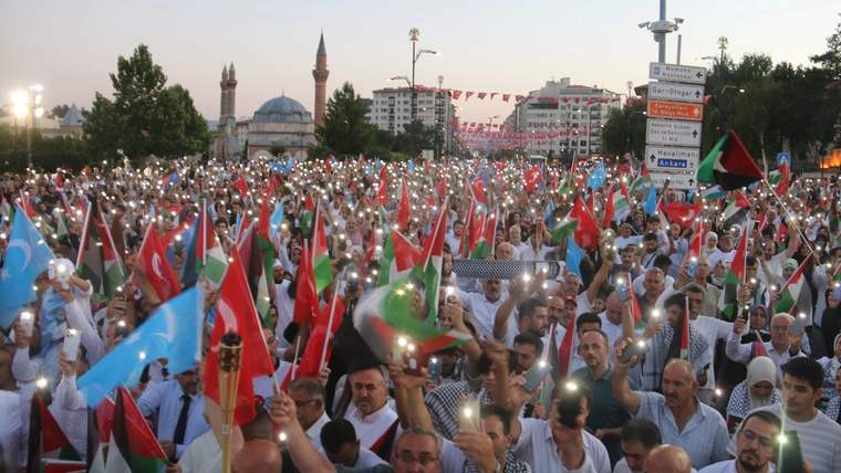 Kalabalık bir grup, Filistin bayrakları ve ışıklar tutarak protesto yürüyüşü yapıyor.