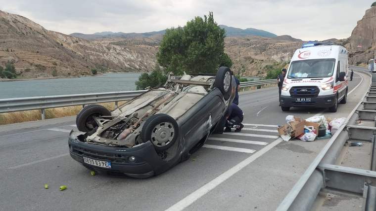 Bölünmüş yolda ters dönmüş bir otomobilin yanında ambulans ve yerde çeşitli eşyalar görülüyor.
