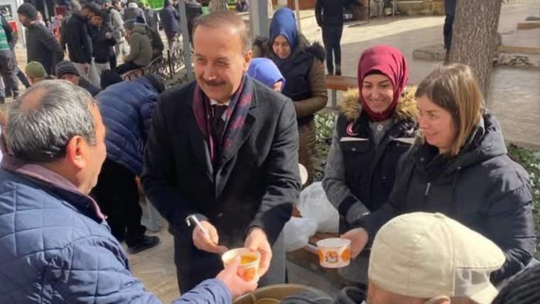 Açık alanda bir adam, çevresindeki insanlara küçük kaplarda yiyecek dağıtırken görülüyor.