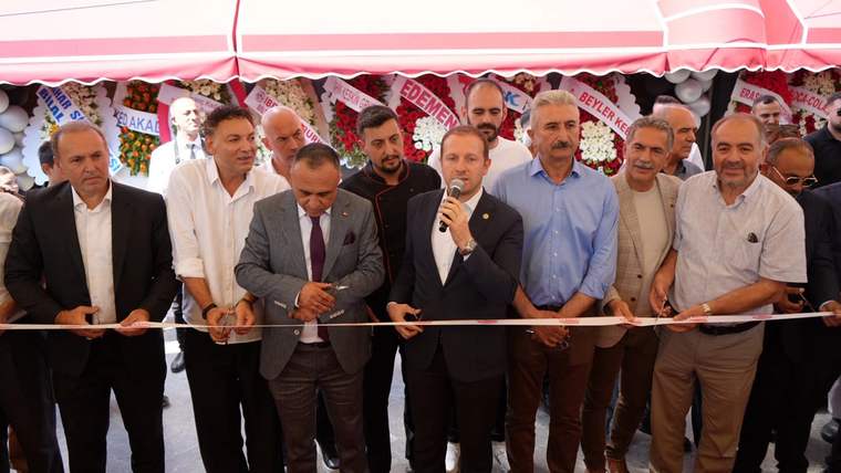 Kırmızı kurdele önünde toplanan bir grup erkekten biri mikrofonla konuşurken diğerleri bekliyor.