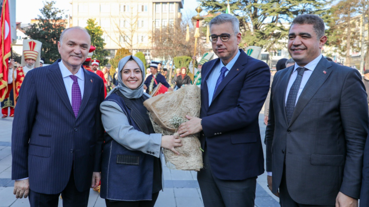 Açık havada dört yetişkin, başörtülü kadının tuttuğu çiçek demetinin etrafında yan yana duruyor.