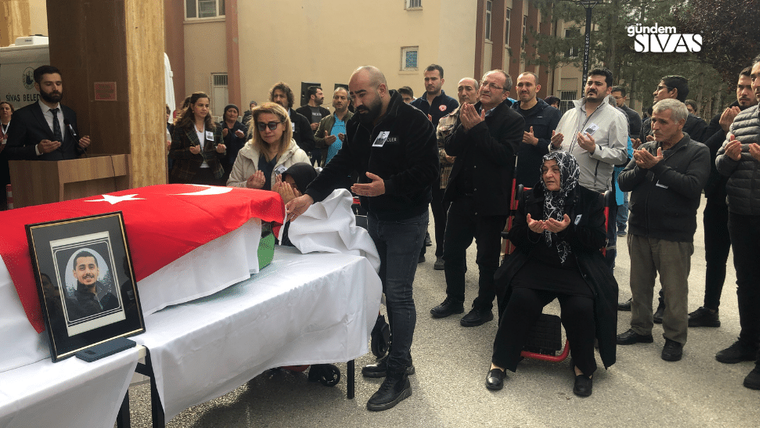 Türk bayrağına sarılı tabutun önünde insanlar, dua ediyor ve ellerini açmış.