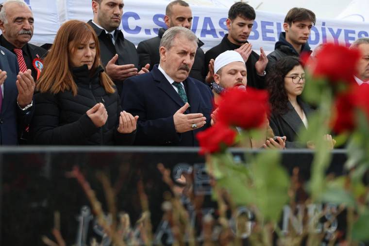 Bir grup insan, mezar başında dua ediyor; ön planda kırmızı güller var.