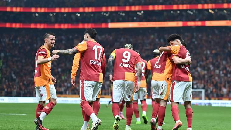 Galatasaray formaları giyen futbolcular, stadyum sahasında yan yana yürüyerek birbirlerine sarılıyor.