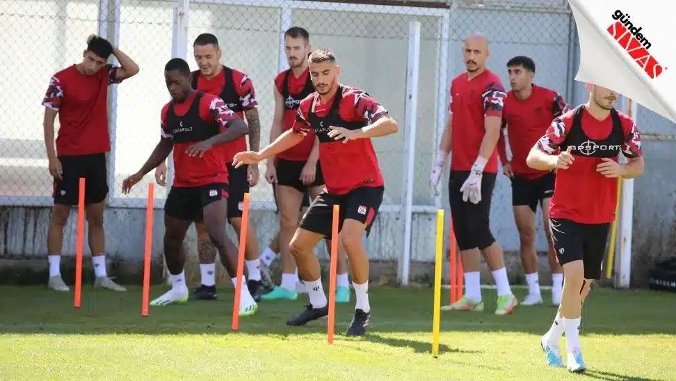 Kırmızı formalar giymiş futbolcular, antrenman sahasında antrenman yapıyor.