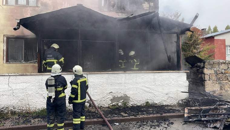 İki katlı bir konutun önünde, yangın söndürme çalışmaları yapan itfaiye ekipleri ve dumanlar.
