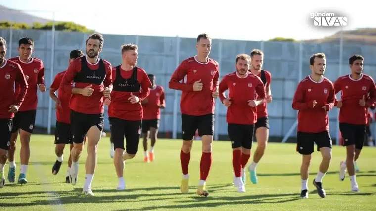 Kırmızı formalar giymiş futbolcular, antrenman sahasında koşu yapıyor.