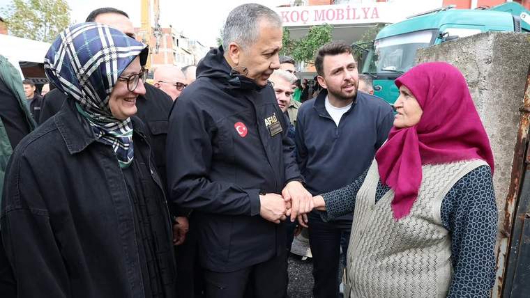Sokakta bir erkekle başörtülü bir kadın el sıkışırken çevrelerinde insanlar ve park edilmiş bir minibüs görülüyor.