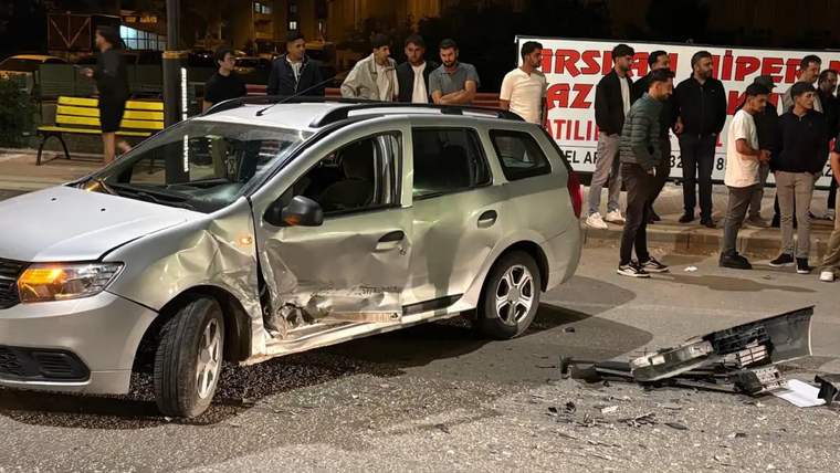 Ön ve yan kısmı hasar görmüş gümüş renkli otomobil, gece saatlerinde yolda duruyor; çevresinde insanlar var.