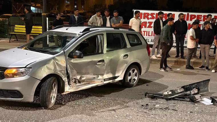 Ön ve yan kısmı hasar görmüş gümüş renkli otomobil, gece saatlerinde yolda duruyor; çevresinde insanlar var.