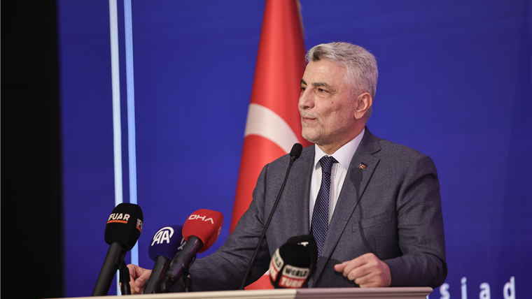 Kürsüde konuşan bir erkek, önündeki basın mikrofonları ve arkasındaki Türk bayrağıyla görülüyor.