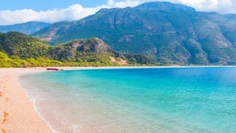 Sakin bir plaj, deniz ve arka planda dağlar görünmekte.