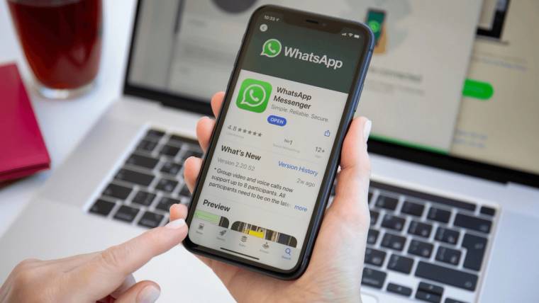 WhatsApp ekranı açık bir akıllı telefon, dizüstü bilgisayarın önünde iki elle tutuluyor.