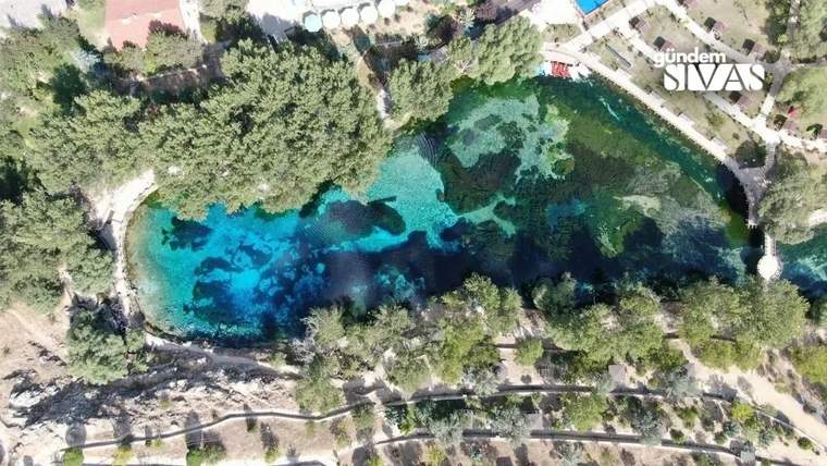 Ağaçlarla çevrili, mavi suyu olan bir göletin üstten görünümü.