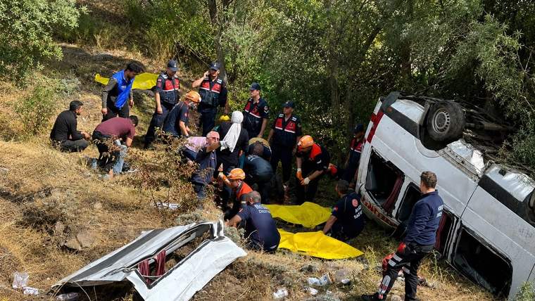 Devrilmiş beyaz minibüsün çevresinde, ağaçlık yamaçta çok sayıda kurtarma görevlisi bulunuyor.
