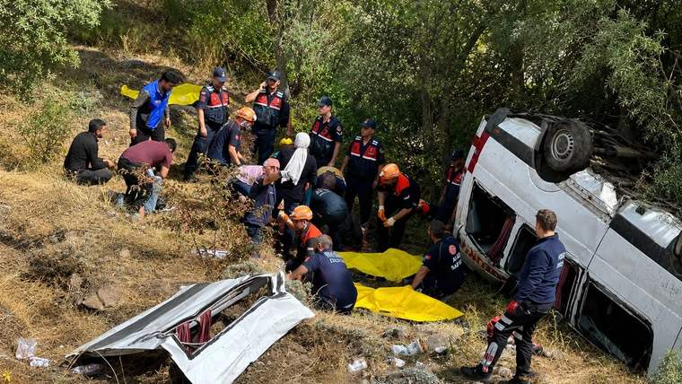 Devrilmiş beyaz minibüsün çevresinde, ağaçlık yamaçta çok sayıda kurtarma görevlisi bulunuyor.