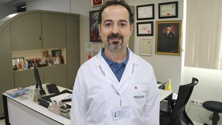 Beyaz önlük giymiş bir doktor, ofisinde gülümseyerek poz veriyor.