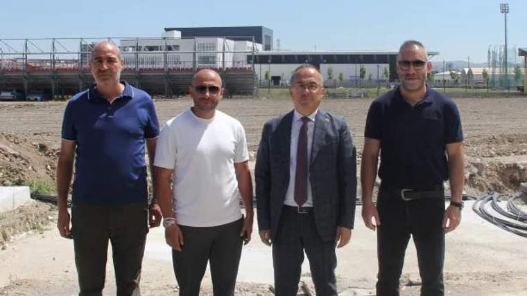 Dört kişi, inşaat alanında yan yana duruyor; arka planda modern bir yapı görünmekte.