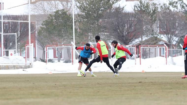 Karlı saha kenarında antrenman yapan üç futbolcu, topun bulunduğu pozisyonda mücadele ediyor.