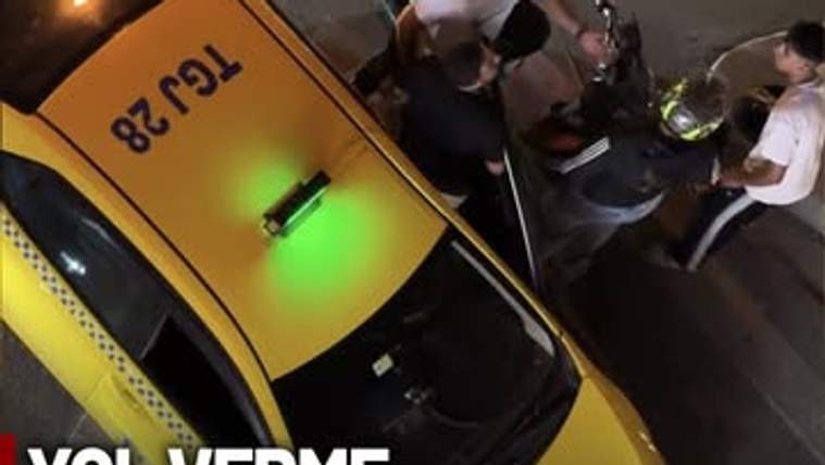 Taksi şoförü ve motosikletli bir kişi, sokakta tartışıyor. Taksi, sarı renkte ve üzerinde 'TC 28' yazıyor.