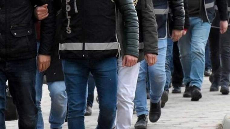 Reflektörlü yelek giyen polisler, kollarından tuttukları kişilerle kaldırımda yürüyor.