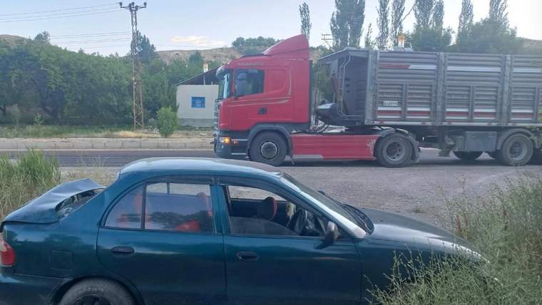 Yolda park halindeki yeşil bir otomobil ve yanından geçen kırmızı bir tır görünüyor.