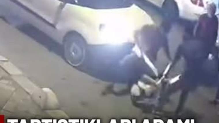 Bir grup kişi, bir adamı yere yatırmış ve sopayla dövüyor. Arka planda bir araç duruyor.