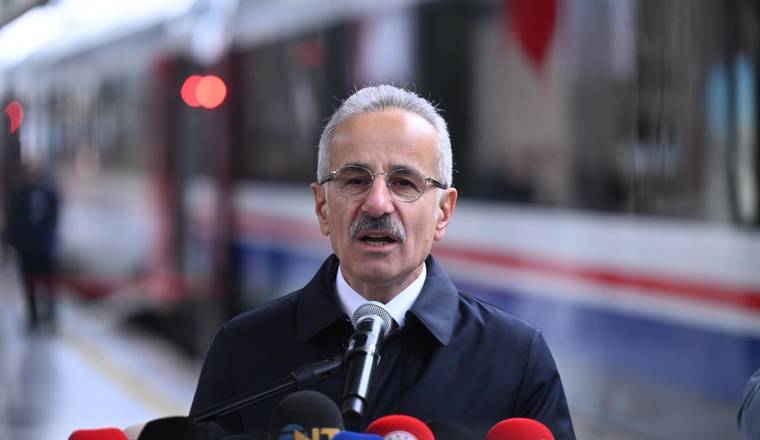 Tren vagonunun önünde, gözlüklü bir kişi mikrofonlara konuşurken görülüyor.