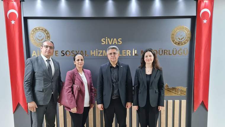 Sivas Aile ve Sosyal Hizmetler İl Müdürlüğü yazılı panonun önünde dört kişi ve iki Türk bayrağı duruyor.