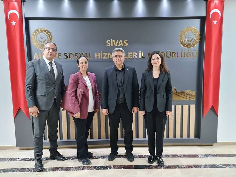 Sivas Aile ve Sosyal Hizmetler İl Müdürlüğü yazılı panonun önünde dört kişi ve iki Türk bayrağı duruyor.
