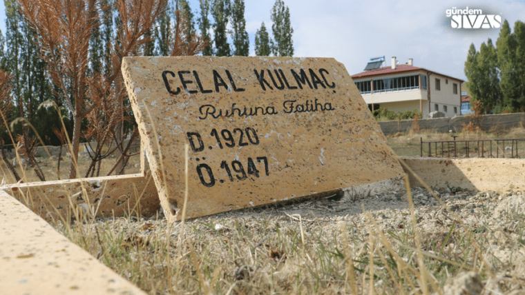 Sarı bir taş üzerinde 'Celal Kulmaç, D.1920, O.1947' yazılı mezar taşı, arka planda ağaçlar ve bir bina görünmekte.