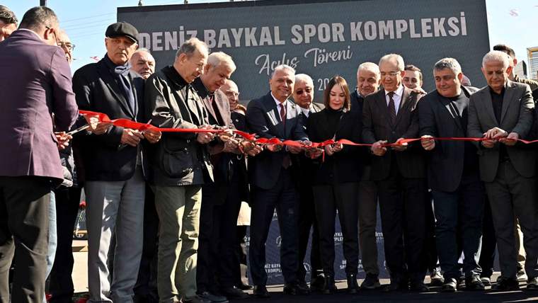 Bir grup kişi, üzerinde Deniz Baykal Spor Kompleksi yazan sahne önünde kurdele kesiyor.
