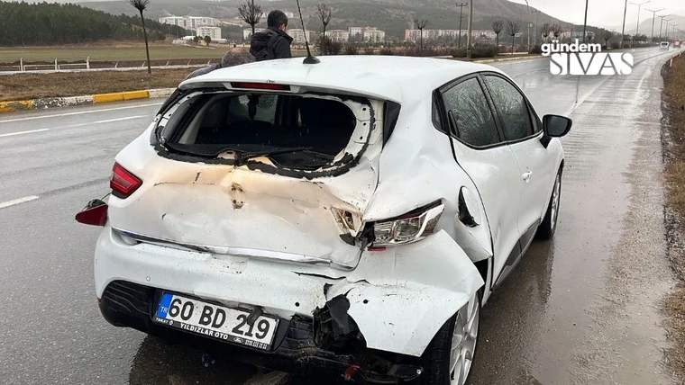 Yağışlı yol kenarında, arka camı kırılmış ve arka bölümü ağır hasar görmüş beyaz otomobil duruyor.