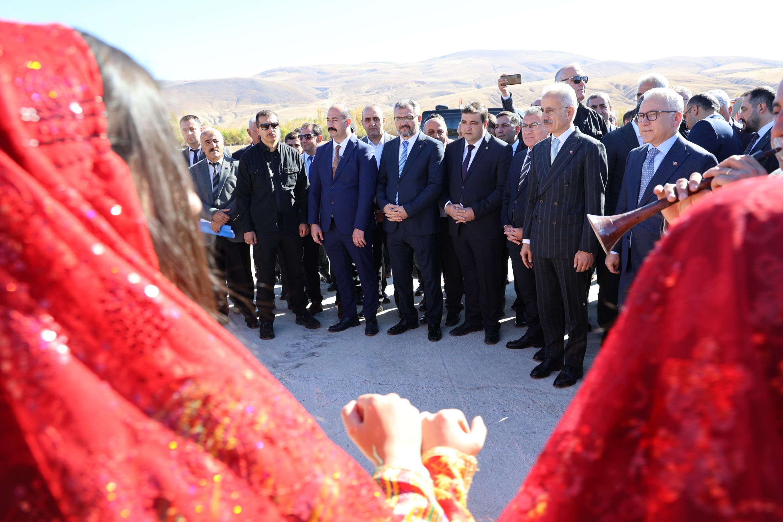 Kırmızı geleneksel kıyafetler giymiş kişiler, bir grup erkeğin önünde duruyor.