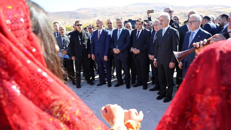 Kırmızı geleneksel kıyafetler giymiş kişiler, bir grup erkeğin önünde duruyor.