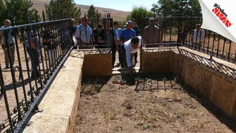 Aşık Veysel'in mezarının etrafında toplanmış bir grup insan, mezara çiçek bırakıyor.
