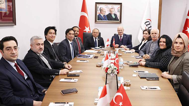 Toplantı masasının çevresinde oturan kişiler, Türk ve Endonezya bayraklarının bulunduğu salonda poz veriyor.