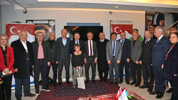 Bir salonda Türk bayraklı afişlerin önünde, aralarında çocuk bulunan kalabalık bir grup yan yana duruyor.