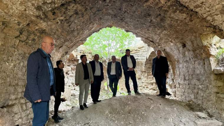 Taş duvarlı kemerli bir yapının içinde ve girişinde duran altı kişi görülüyor.