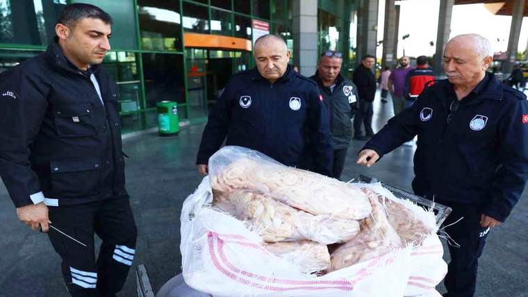 Üç görevli, bina girişinde büyük bir çuval içindeki poşetlenmiş et parçalarının yanında duruyor.