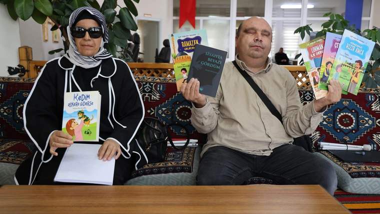 Görme engelli bir kadın ve bir adam, kitaplarını tutarak oturuyor. Arkada Türk bayrağı görünmekte.