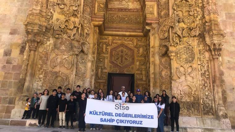 Süslü taş kapı önünde bir grup öğrenci, üzerinde kültürel değerlere sahip çıkma mesajı bulunan pankart tutuyor.