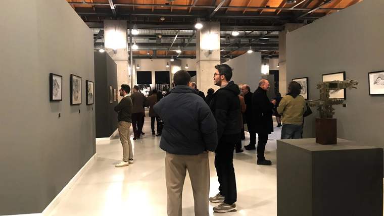 Galeri salonunda duvarlardaki tabloları ve sergilenen heykelleri inceleyen ziyaretçiler görülüyor.