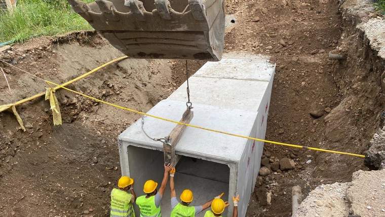 Sarı baretli dört işçi, kazı alanında beton bir yapının vinçle yerleştirilmesine eşlik ediyor.