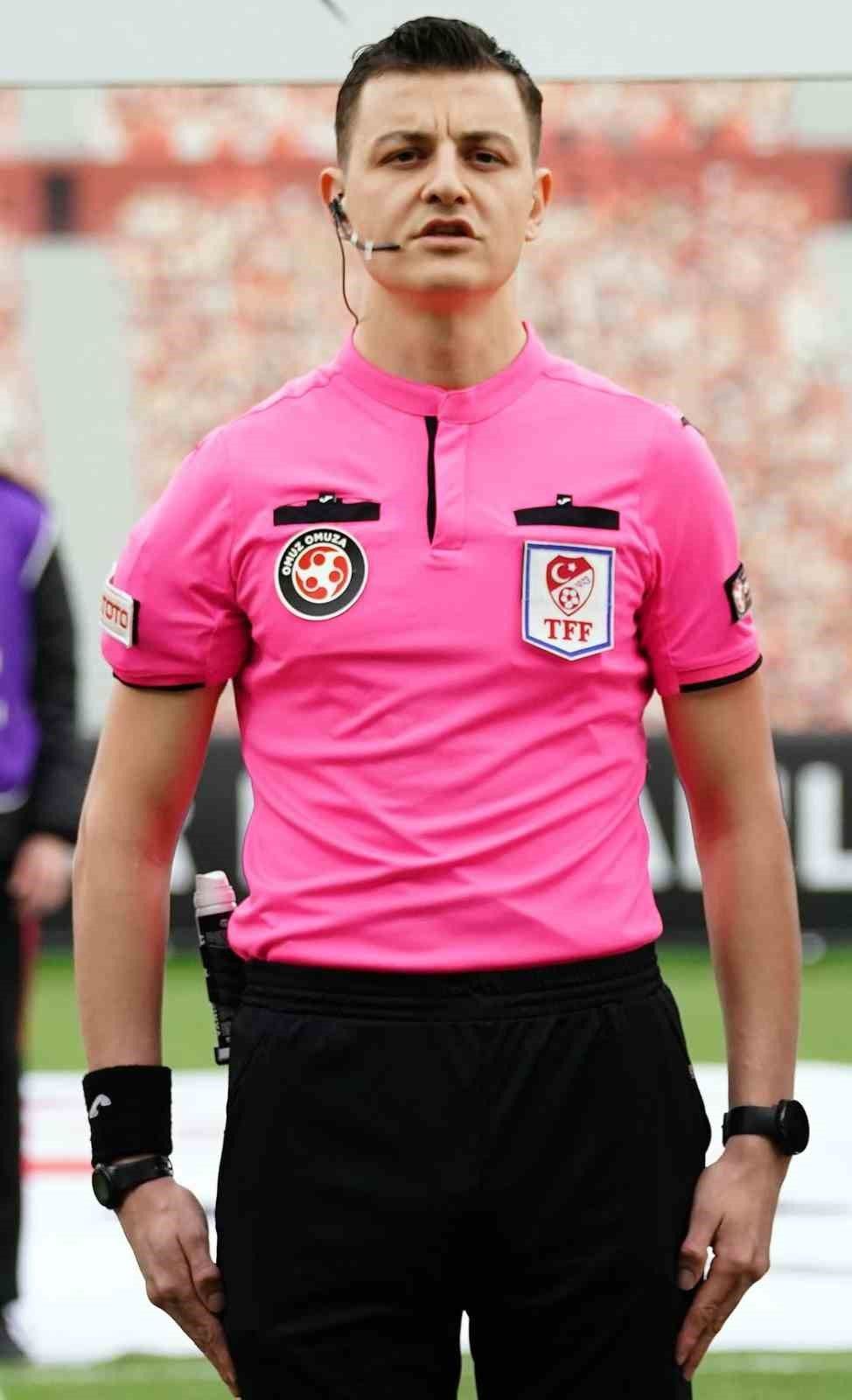 Pembe forması üzerinde hakem ve TFF armaları bulunan bir hakemin gövdesi, saha kenarında görülüyor.