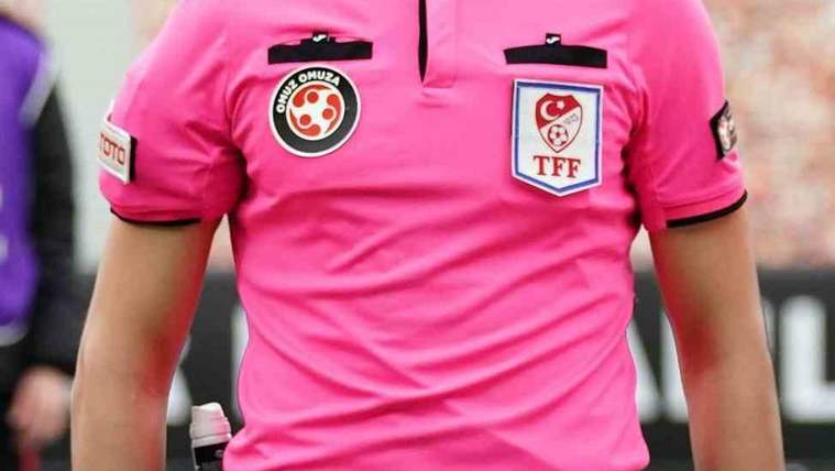 Pembe forması üzerinde hakem ve TFF armaları bulunan bir hakemin gövdesi, saha kenarında görülüyor.